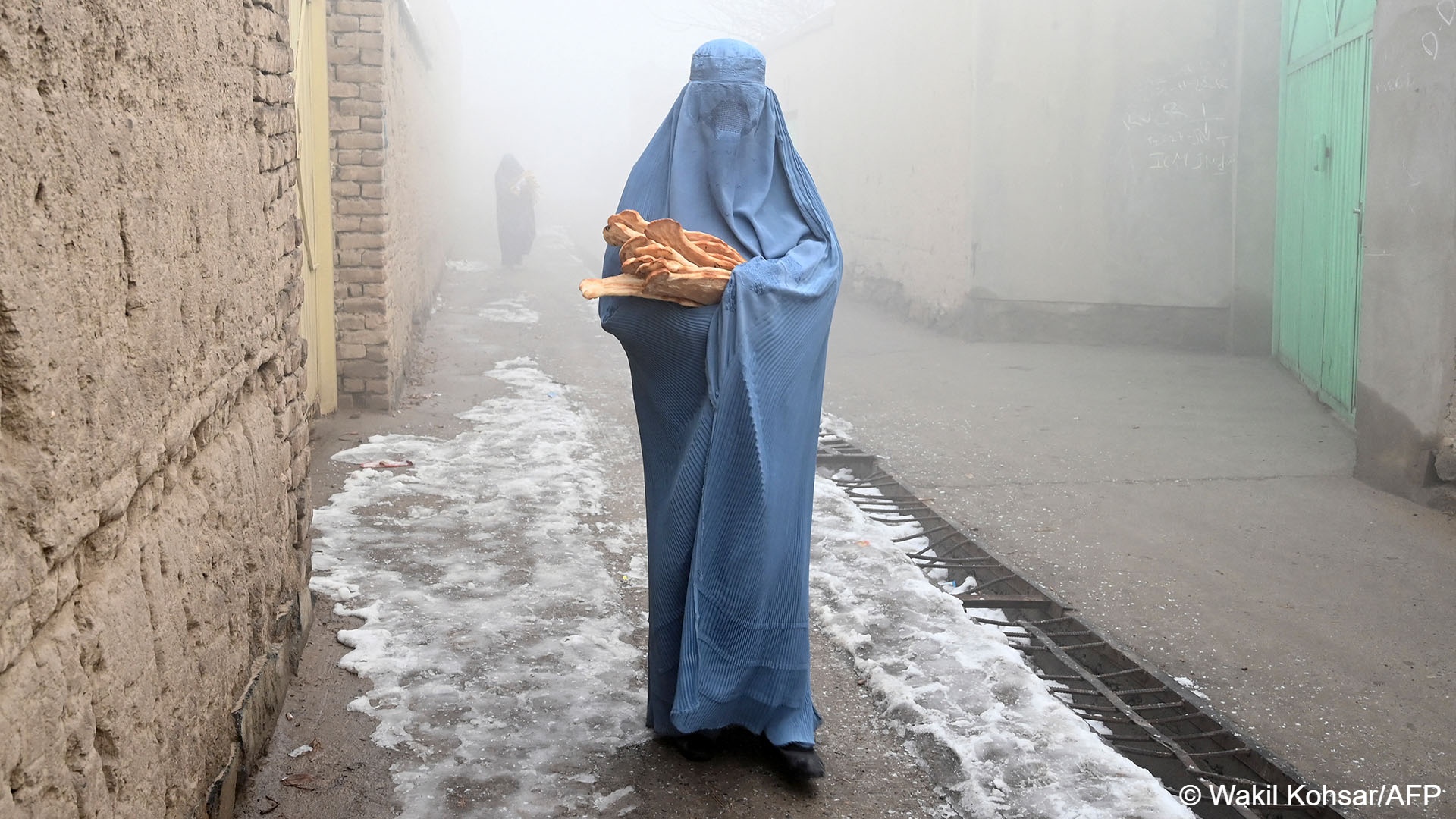A woman wearing a burka walks along a road towards her home after receiving free bread distributed as part of the Save Afghans From Hunger campaign in Kabul on 18 January 2022.
