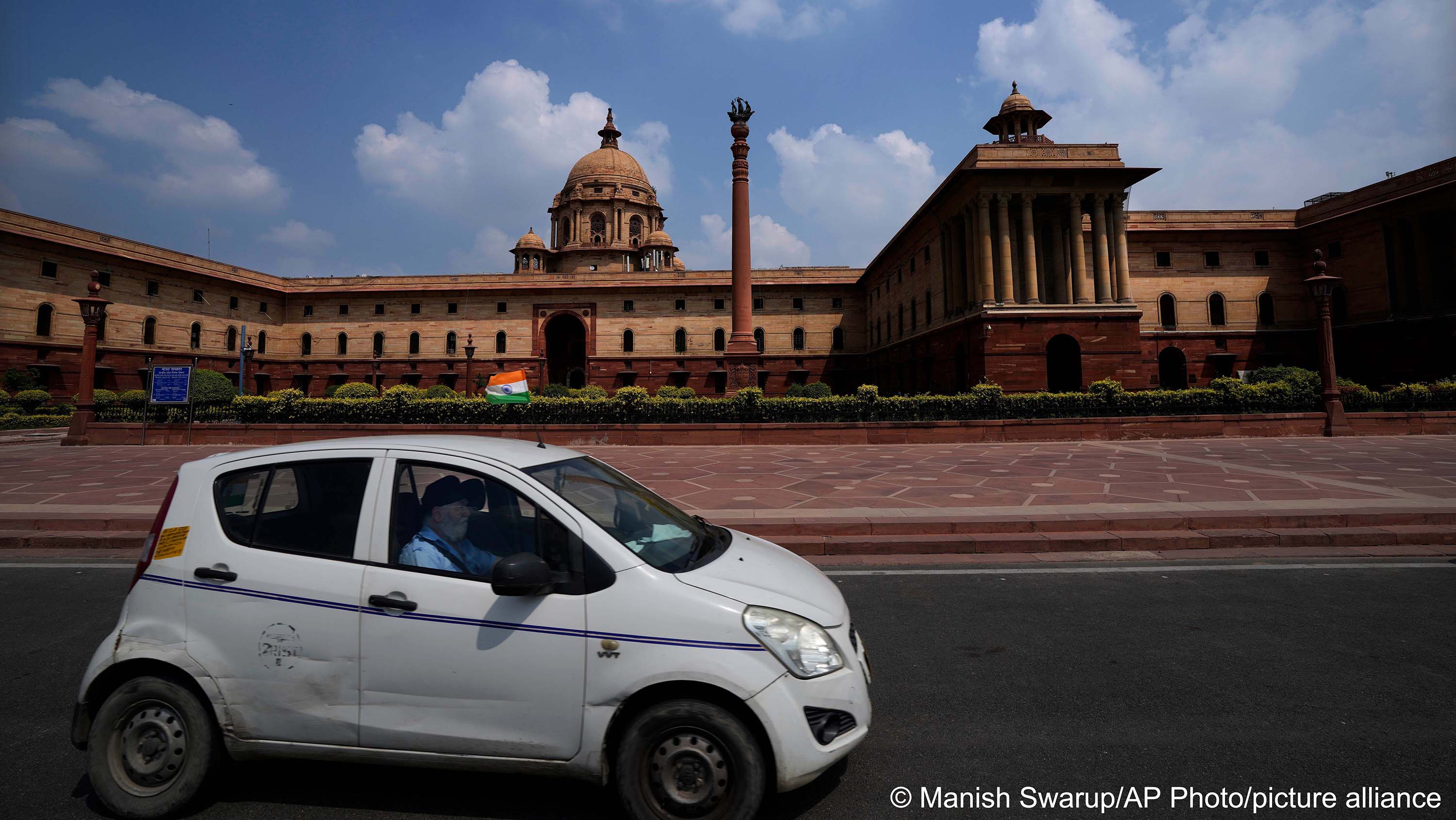 A taxi carrying the national flag drives past a colonial building which houses important ministries in New Delhi, India, 11 September 2022 (photo: AP Photo/Manish Swarup)