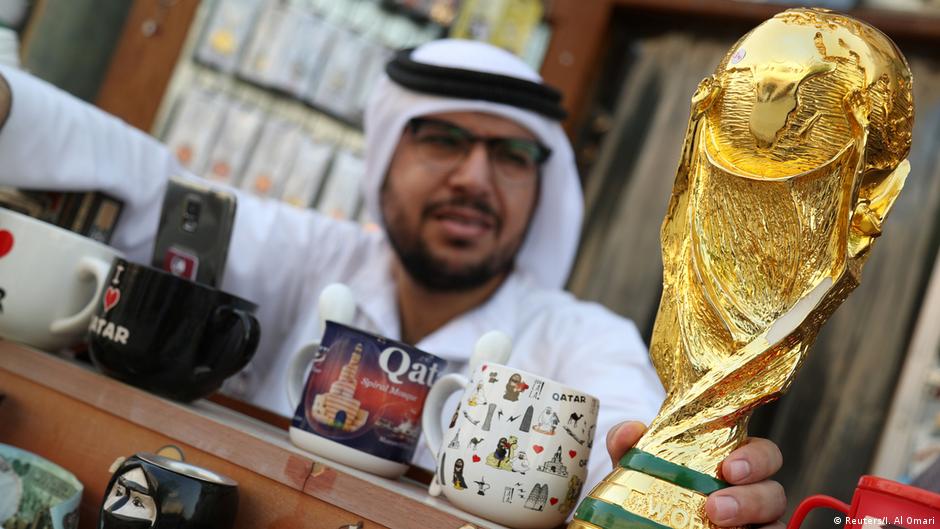 عربي يحمل نموذجا بالحجم الطبيعي لكأس العالم - كرة القدم  - في متجر للهدايا التذكارية.