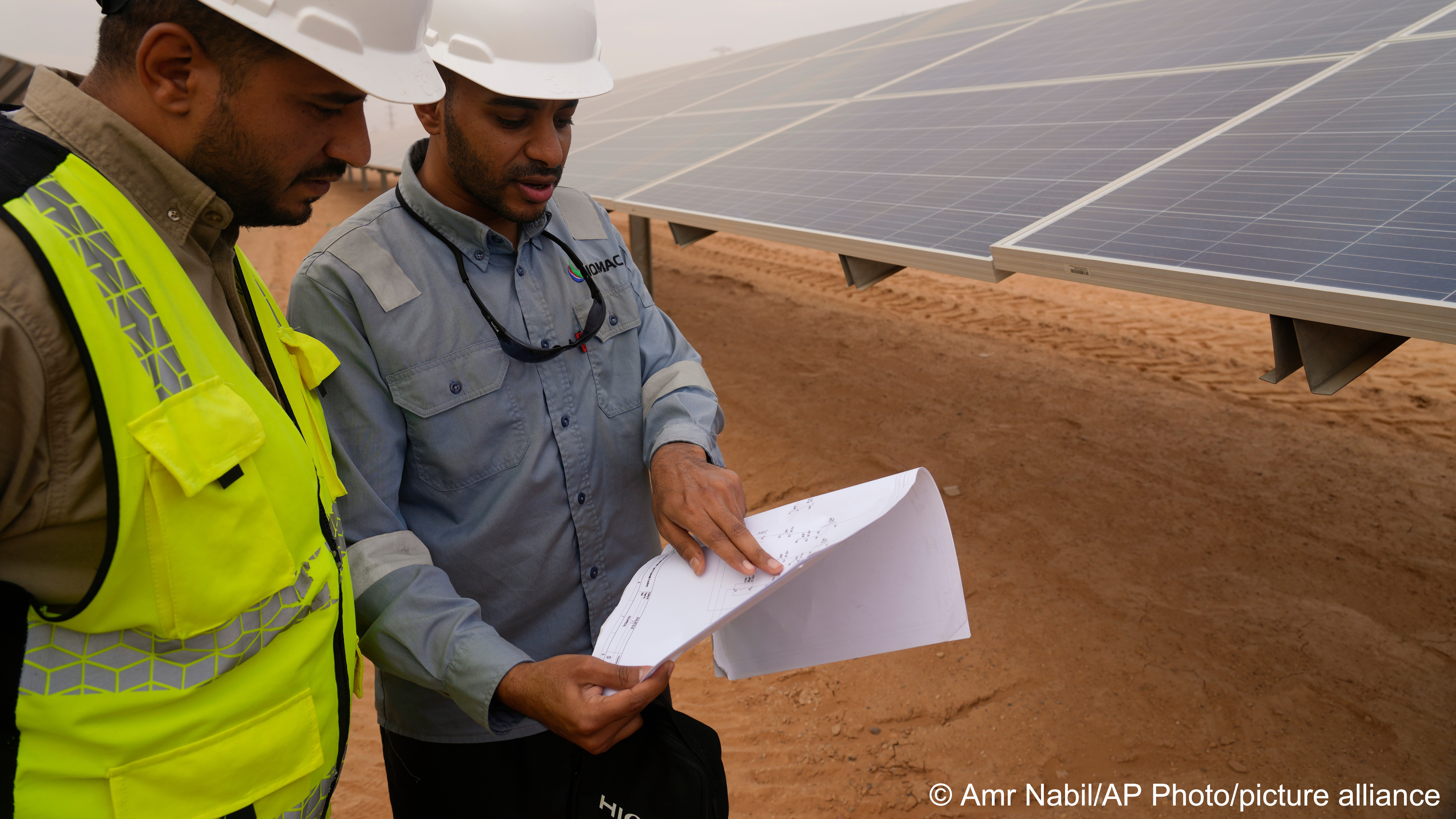 Engineers talk next to photovoltaic solar panels at Benban Solar Park, one of the world’s largest solar power plants in the world, in Aswan, Egypt, 19 October 2022 (photo: AP Photo/Amr Nabil)