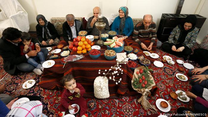 A family sits with plates around a set table on the floor for the festival of Yalda