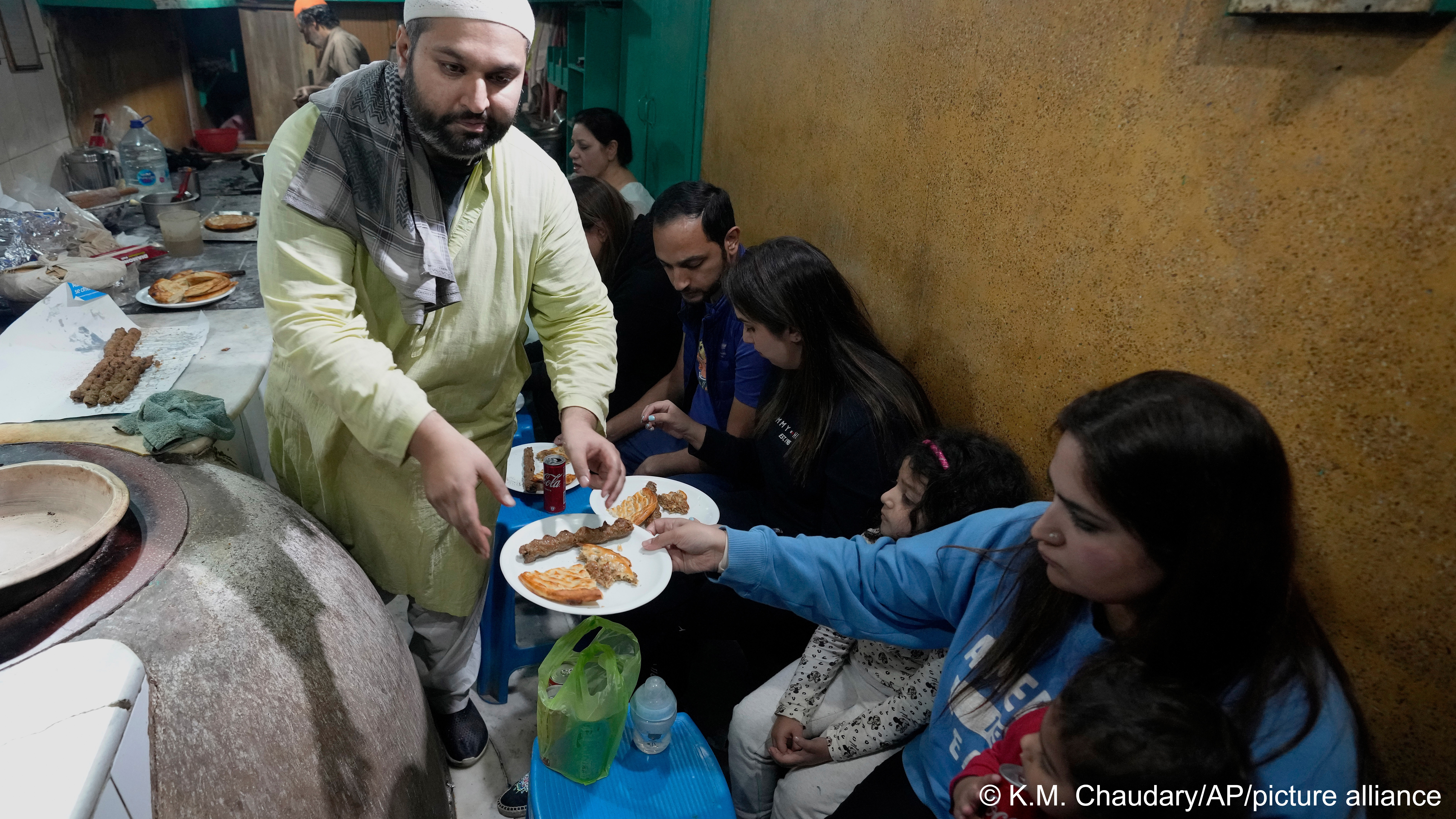 Bilal Sufi, left, owner of Baking Virsa eatery, serves traditional kebabs and naan bread in Lahore, Pakistan, 3 December 2022 (photo: AP Photo/K. M. Chaudary)