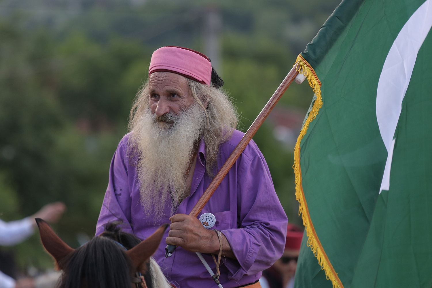 A white-haired, bearded man carrying a flag and wearing purple rides on horseback (photo: Konstantin Novakovic)