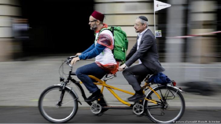 A rabbi and an imam on a tandem bicycle cycling down a street in Berlin (photo: picture-alliance/AP Photo/M. Schreiber)
