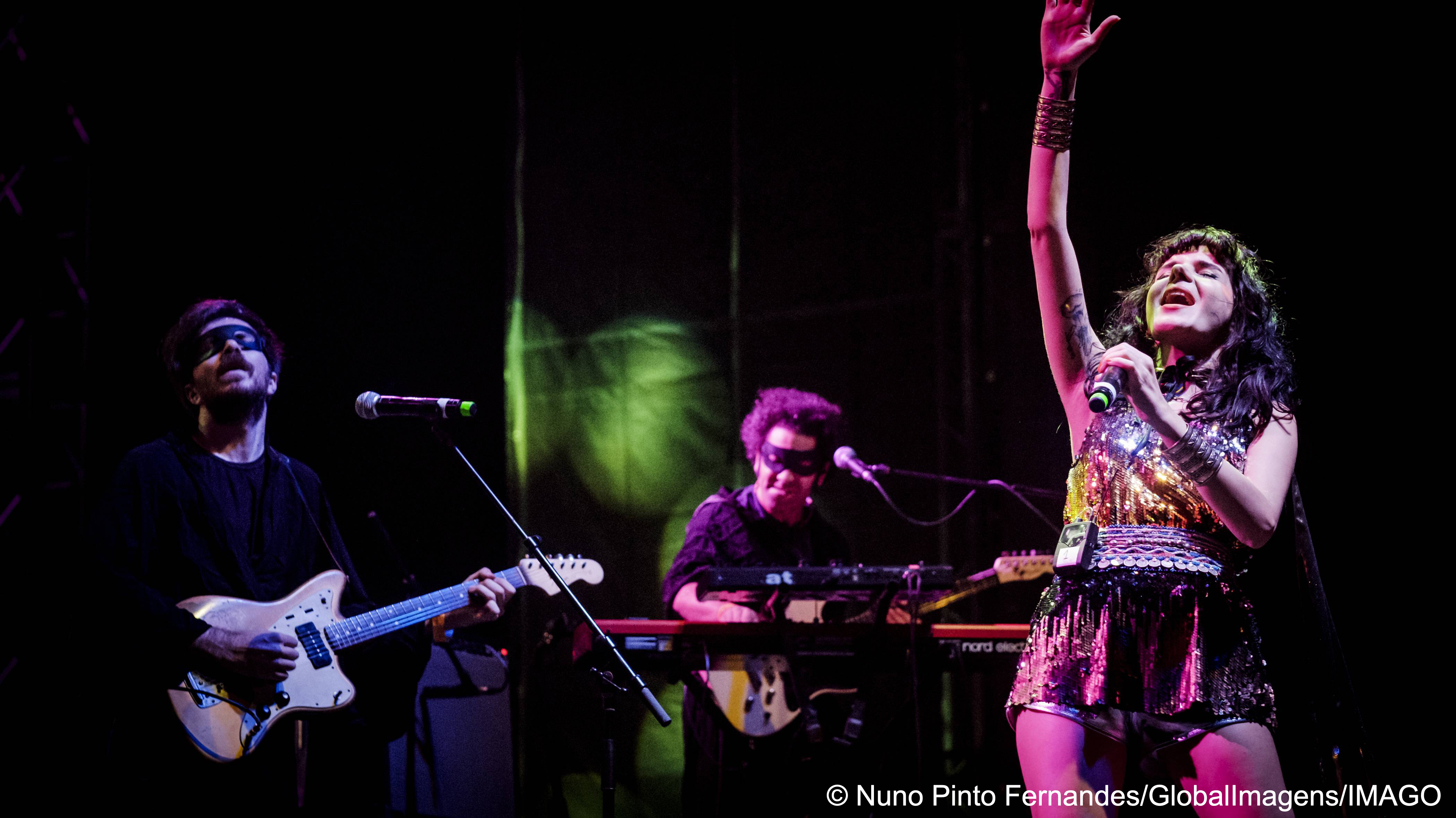Gaye Su Akyol streckt ihren rechten Arm in die Luft während sie zusammen mit zwei maskierten Musikern auf der  Bühne singt (Foto: Nuno Pinto Fernandes/GlobalImagens/IMAGO)