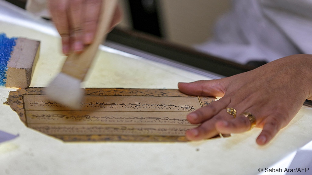 A conservator uses a brush on a Persian-language manuscript undergoing restoration at the House of Manuscripts in Baghdad (image: Sabah ARAR/AFP)