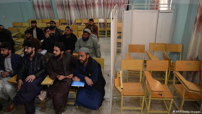 On the left of the picture, a group of male students apparently taking part in a seminar. On the right, separated by a curtain, are six empty chairs.