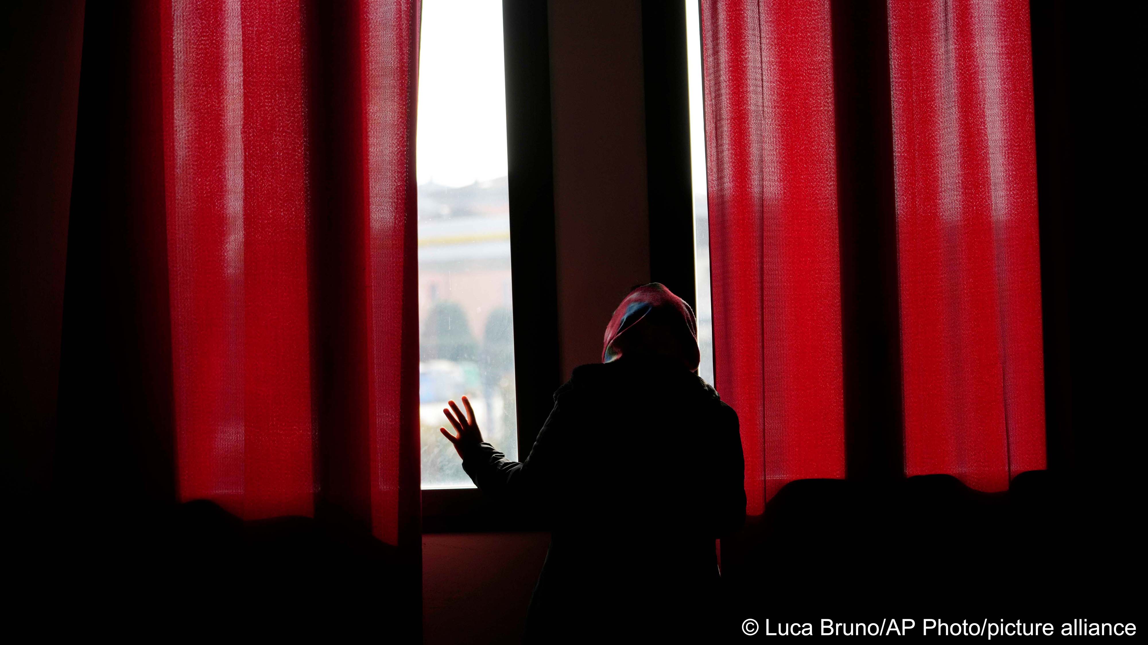 Pakistani-born Iram Aslam, 29, peeks through the window of a local social activities centre in Guastalla, northern Italy, 11 February 2023, during an interview with The Associated Press (image: Luca Bruno/AP Photo/picture alliance) 