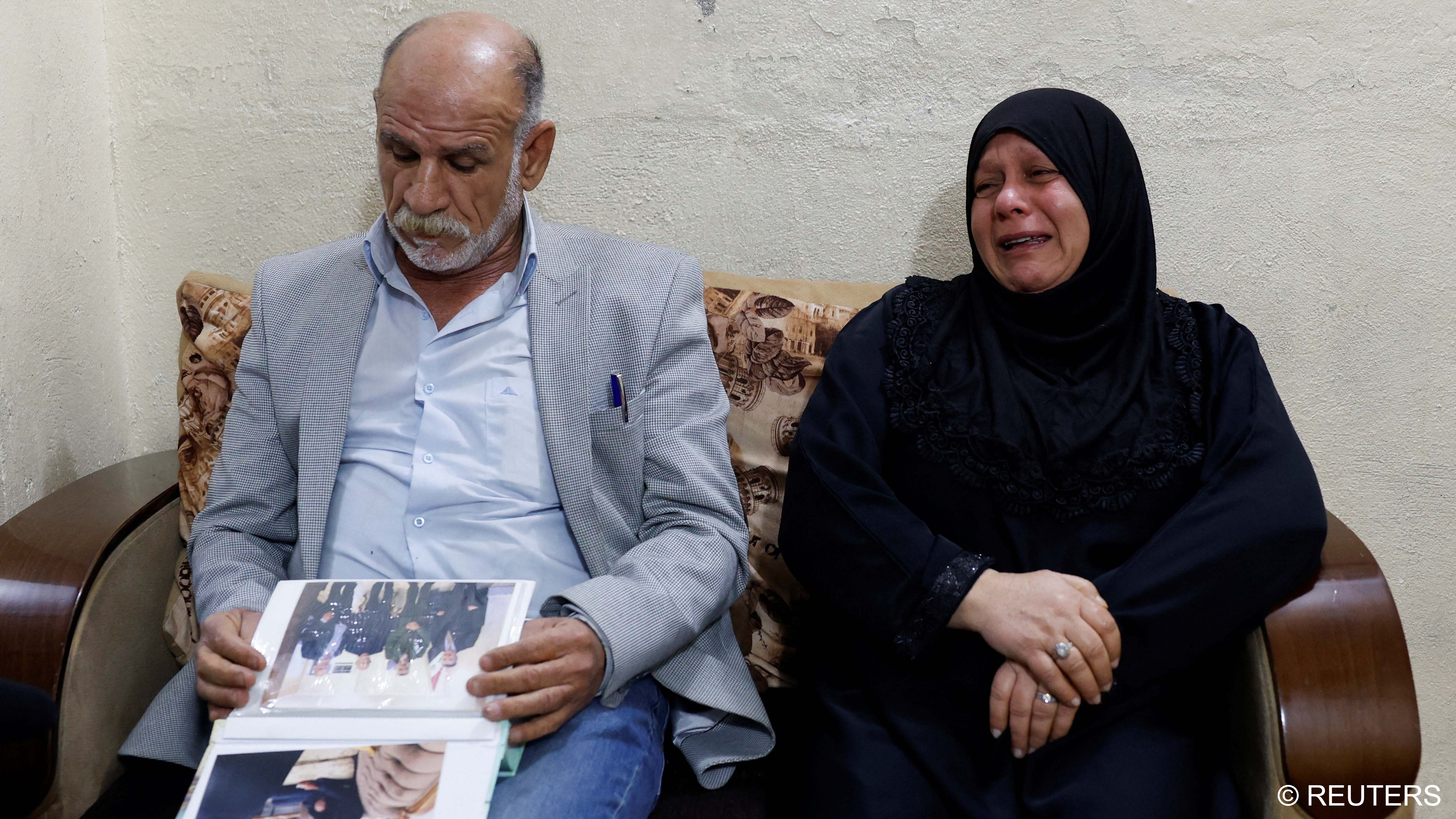Majid Mohammed looks at pictures of his son who disappeared after the Camp Speicher massacre in 2014, where some of the hundreds of Iraqi military recruits who were abducted from Camp Speicher by Islamic State militants in June 2014 are believed to have been murdered, as his wife, Nadia Jasim, reacts during an interview with Reuters, in Baghdad, February 2023 (image: Reuters)