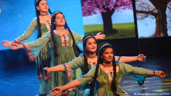 Four women in green dance with outstretched arms in front of a projection showing a tree in flower