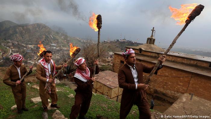 Four men in traditional costume carry burning brands up a hillside.