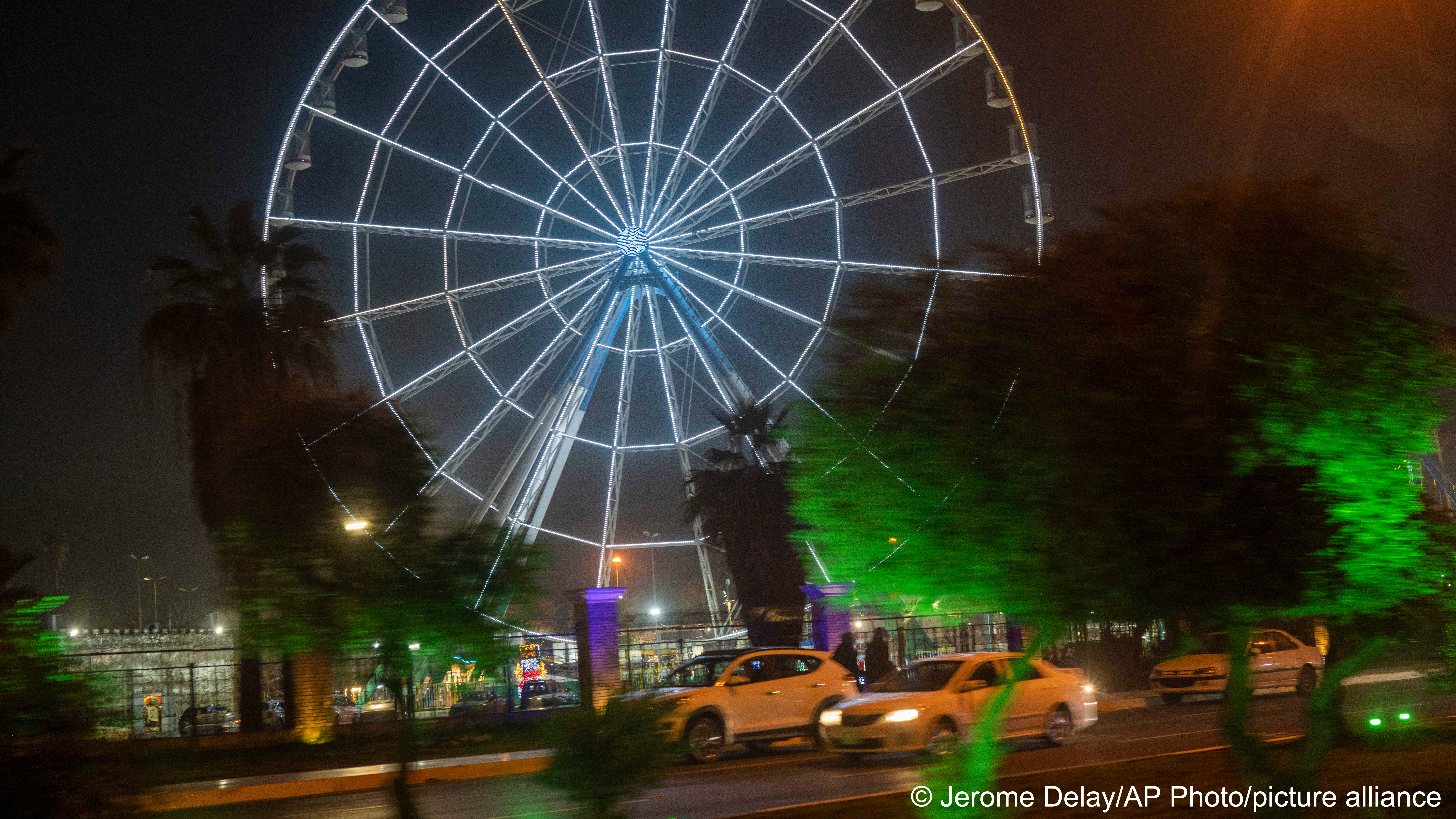 The ferris wheel of Baghdad’s Alzawraa amusement park shines in the night  in Baghdad, Iraq, Friday, Feb. 24, 2023. Two decades after a U.S.-led  invasion, Iraq’s capital today is full of life and a sense of renewal, its  residents enjoying a hopeful, peaceful interlude in a painful modern history (image: AP Photo/Jerome Delay)