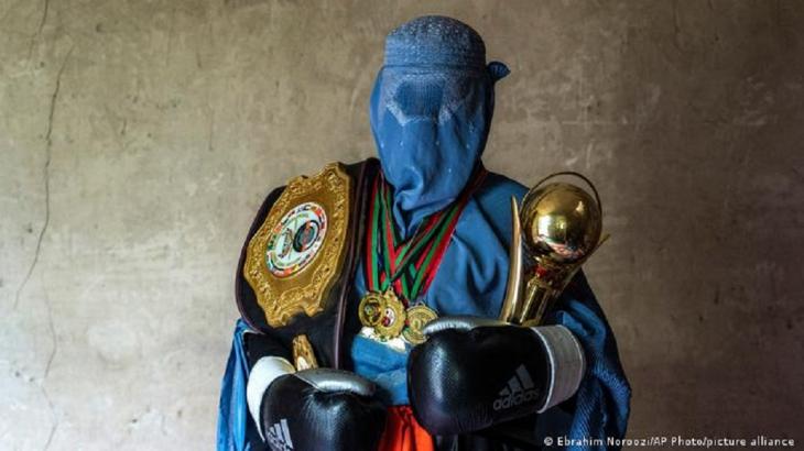 A woman in a burka and boxing gloves poses with her medals and trophies