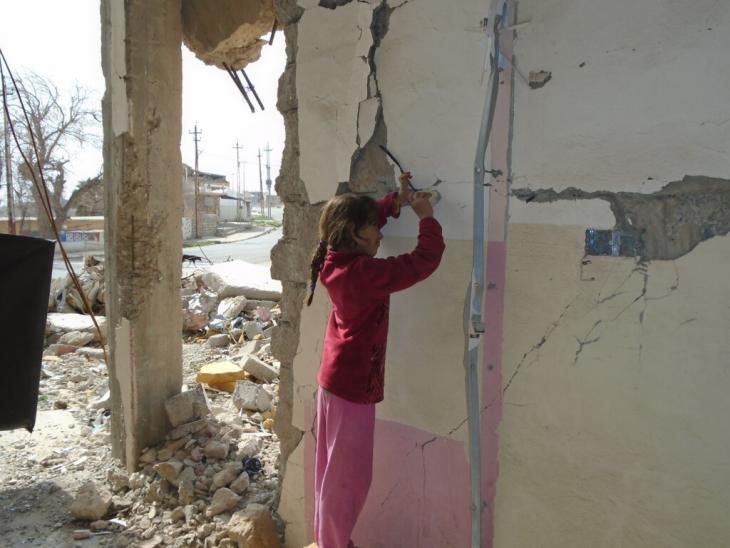 A young girl tries to remove some metal from the wall of a ruined building in the city of Sinjar to sell for cash (photo: Birgit Svensson)