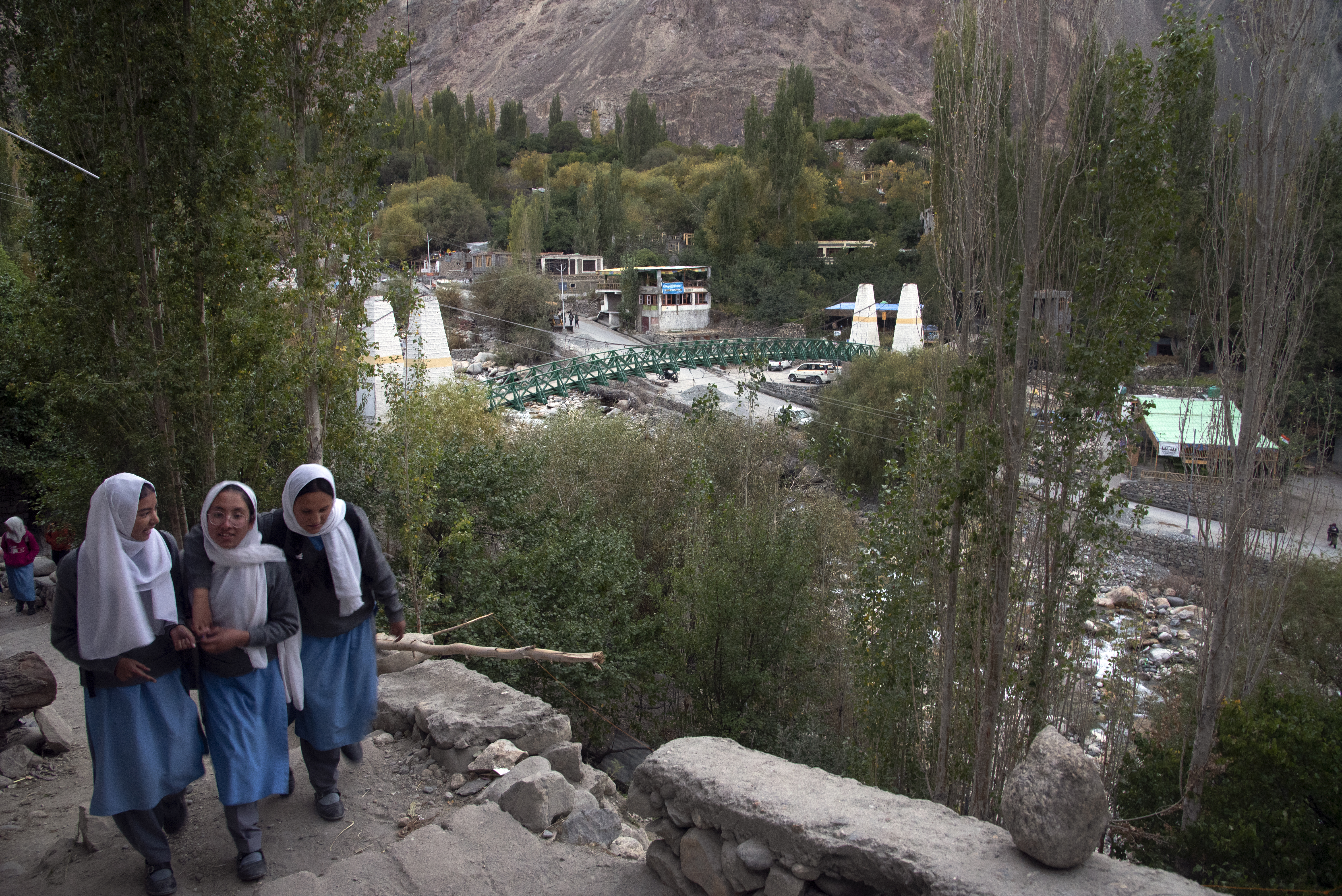 A group of girls walks along a mountain path with a ravine behind them, a river and bridge below (image: Sugato Mukherjee)