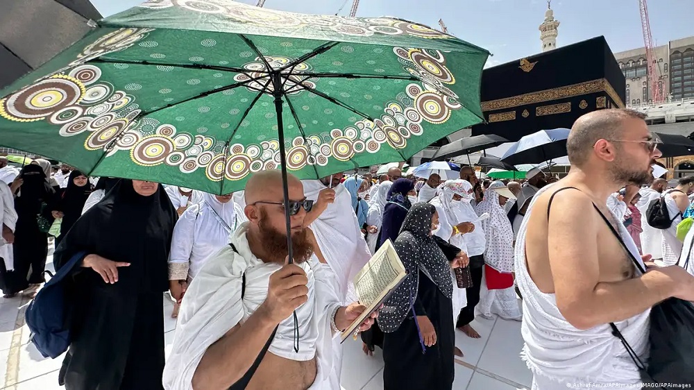 Ein Pilger in Mekka schützt sich vor der Sonne mit einem Schirm, zugleich liest er den Koran. (Foto: Ashraf Amra/APAimages/IMAGO/APAimages)