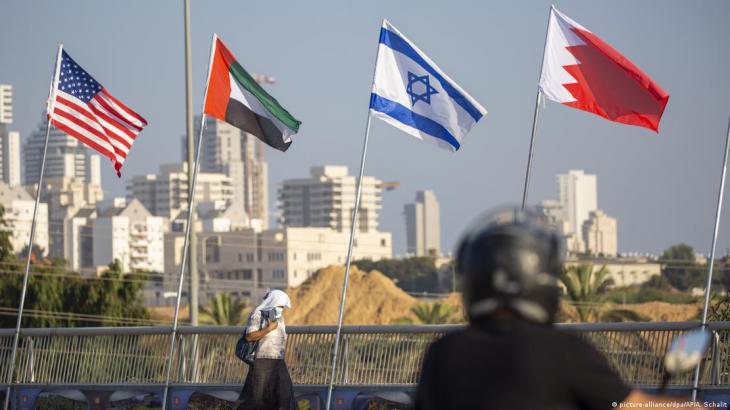 A woman wearing a mask walks past the flags (left–right) of the United States, the United Arab Emirates, Israel and Bahrain, Netanja, Israel, 14 September 2020 (photo: Picture-alliance/dpa/AP/A. Schalit)