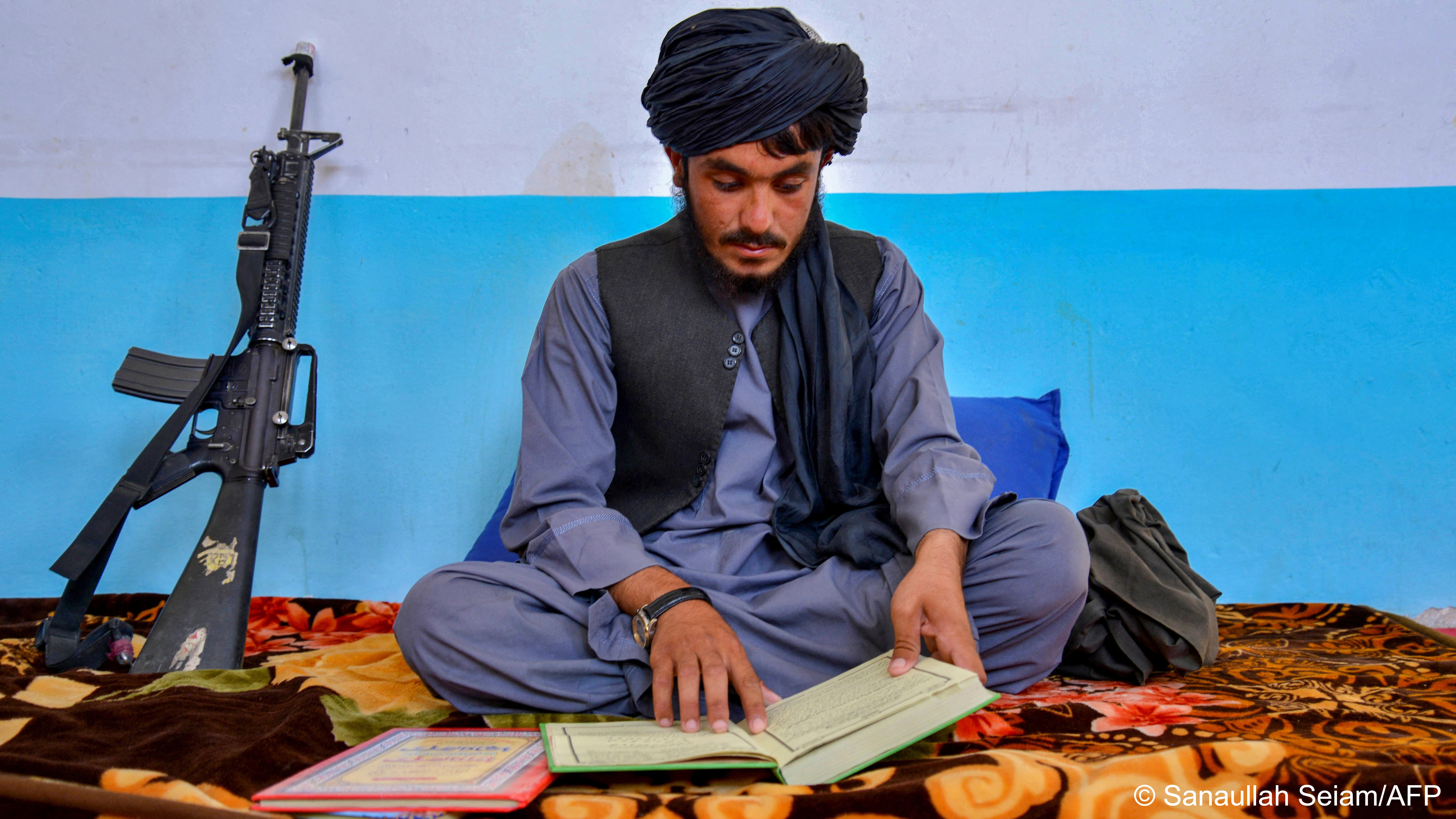 Taliban policeman Lal Muhammad reads a religious book at the police headquarters in Dand district of Kandahar province on 1 August 2023 (image: Sanaullah Seiam/AFP)