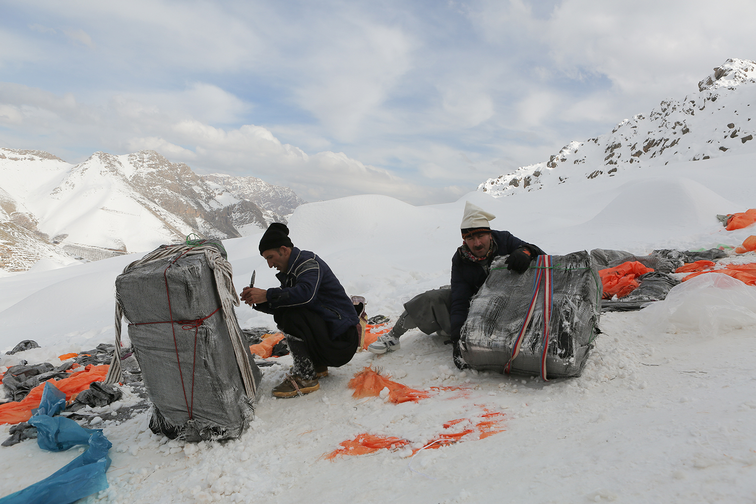 Umgeben von Bergen gehen zwei Männer in die Hocke, um sich um ihre Rucksäcke zu kümmern; Foto: Konstantin Novakovic