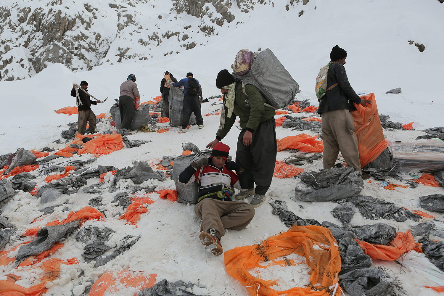 Rucksäcke und orangefarbenes Plastik liegen auf dem schneebedeckten Boden verstreut. Männer arbeiten; Foto: Konstantin Novakovic