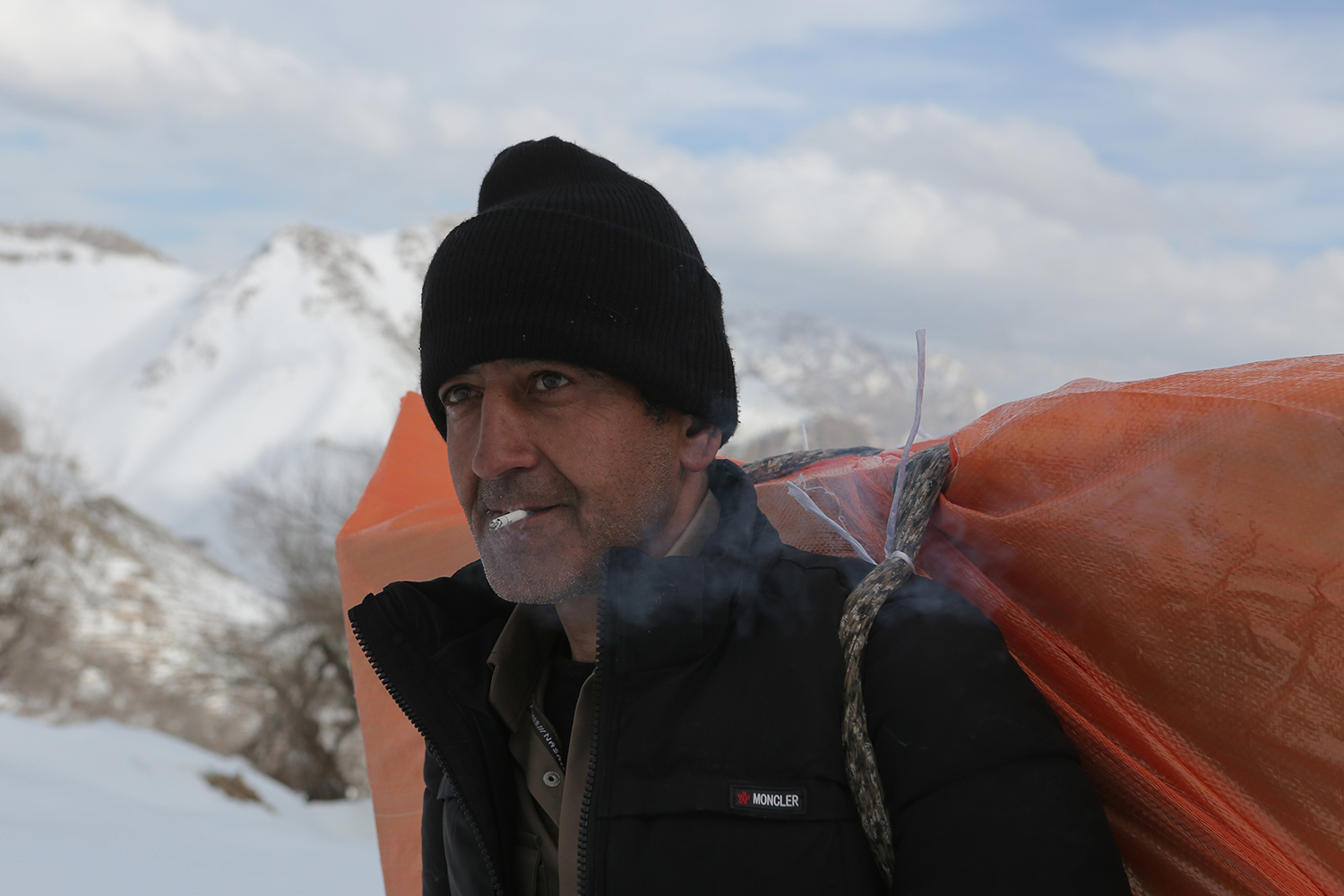 Mann mit Wollmütze raucht eine Zigarette mit Bergen im Hintergrund; Foto: Konstantin Novakovic