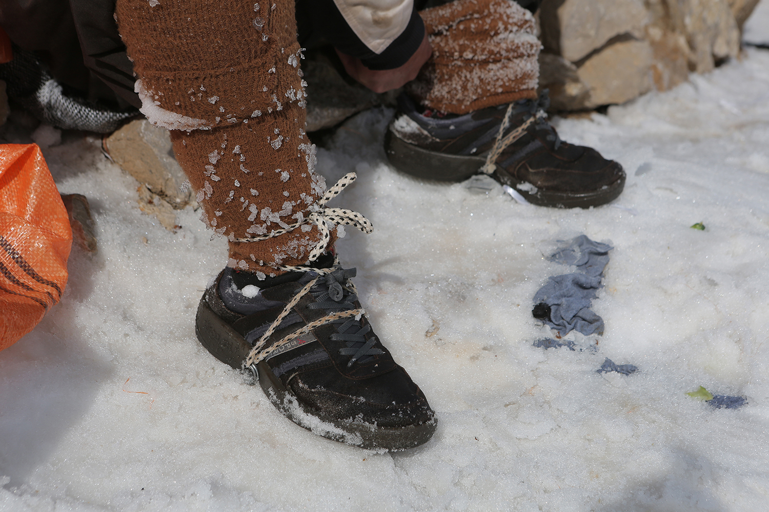 Nahaufnahme von schlecht beschuhten Füßen im Schnee mit behelfsmäßigem Seil und Metallsteigeisen; Foto: Konstantin Novakovic