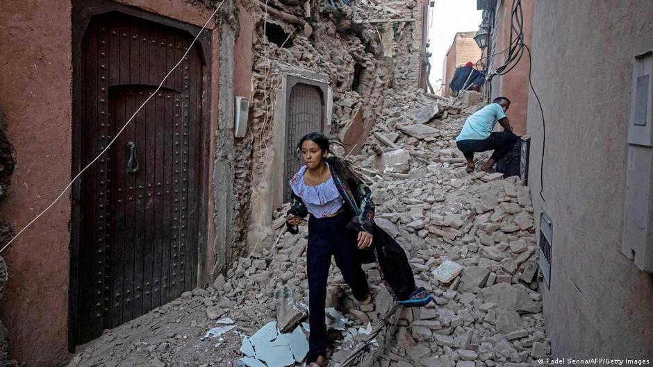 A woman walking through the rubble in a narrow earthquake-damaged street