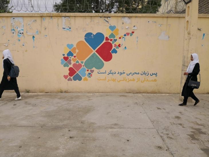 Two girls wearing white hijabs walk past a wall painted with coloured hearts, Balkh, Afghanistan (image: Marian Brehmer)