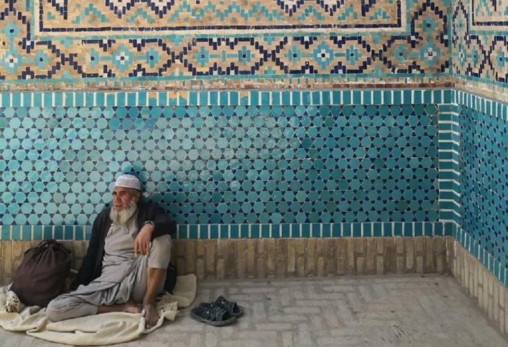 A man sits on a white blanket in front of a tiled wall outside the Green Mosque, Balkh, Afghanistan (image: Marian Brehmer)
