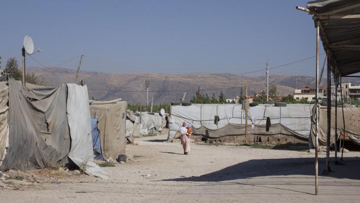 A woman walks between tarpaulin-covered shacks in an informal settlement inhabited by Syrian refugees near the city of Bar Elias, Beqaa Valley, Lebanon (image: Andrea Backhaus)