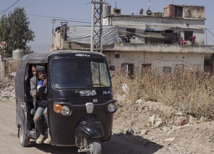 Three Syrian refugees in a black auto rickshaw travel along a dusty road near the city of Bar Elias, Beqaa Valley, Lebanon (image: Andrea Backhaus)