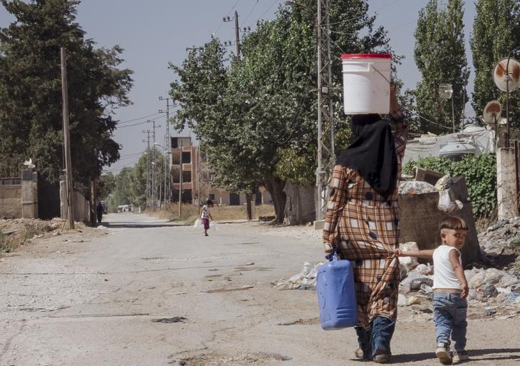 Women and children carry canisters of water along a dusty road near the city of Bar Elias, Beqaa Valley, Lebanon (image: Andrea Backhaus)