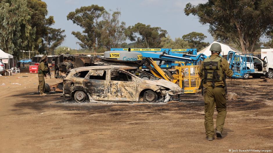 Soldiers stand near a burnt-out vehicle 