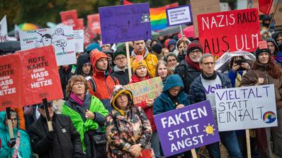 A crowd holding signs and banners demonstrate against the far right.