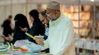 A man at a book fair reads the back of a book he is holding.