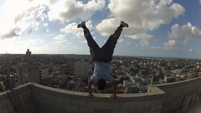 A man performs a handstand on the edge of a building overlooking a city in Gaza.