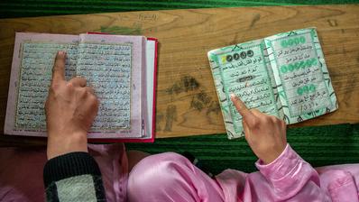 Two people point their fingers at two copies of the Qur'an. Photo from above, only the hands visible.
