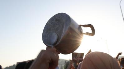 A pot is held up, the other hand holds a spoon