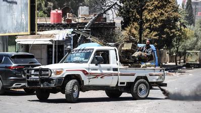 A pickup truck with a man seated behind a weapon, which is mounted on the truck.