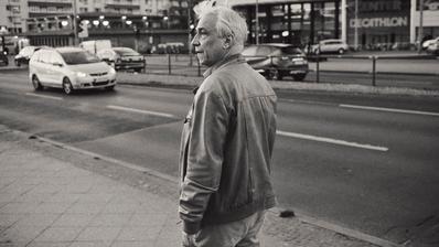 Ein Mann in Lederjacke vor einer befahrenen Straße, in schwarz-weiß.