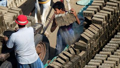 طفل وبجواره رجل يضعان قطع الطوب على عربة يجرها حمار.