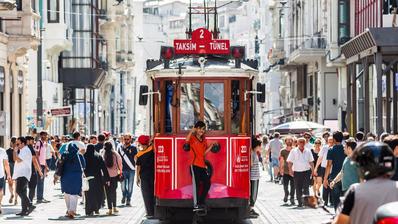 Ein kleiner Junge zeigt den Daumen nach oben, er fährt hinten auf einer roten Tram durch eine belebte Straße.