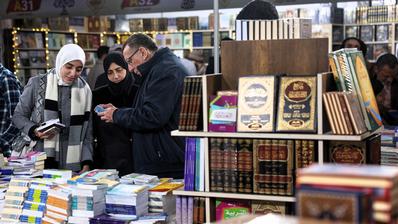 Mehrere Personen schauen sich Bücher an, im Vordergrund ein Bücherregal. 