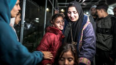 A woman is holding two little girls in her arms amid a crowd of people.