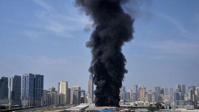 A column of black smoke rises from a city.