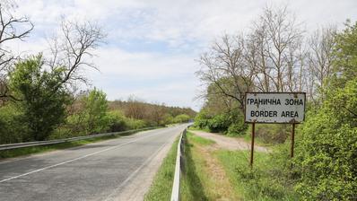 A road; to the right of it is a sign bearing the words "Border Region" in English and Bulgarian.