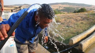 A man is holding a garden hose over his head, with a vast landscape behind him.