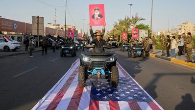 عناصر من قوات الحشد الشعبي العراقية يحملون صورة لآية الله علي خامنئي أثناء مرورهم فوق علم أمريكي في بغداد، 1 أكتوبر/تشرين الأول 2026.