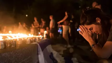 People kneel in grief in front of a sea of lit candles