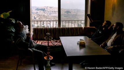 Palästinenser in einem Café in der Stadt Bethlehem. Im Hintergrund die israelische Siedlung Har Homa im besetzten Westjordanland, 7. Dezember 2023. Israel hat den Bau weiterer 1700 Wohnungen im Westjordanlandgenehmigt, gab eine Nichtregierungsorganisation am 6. Dezember 2023 bekannt. 